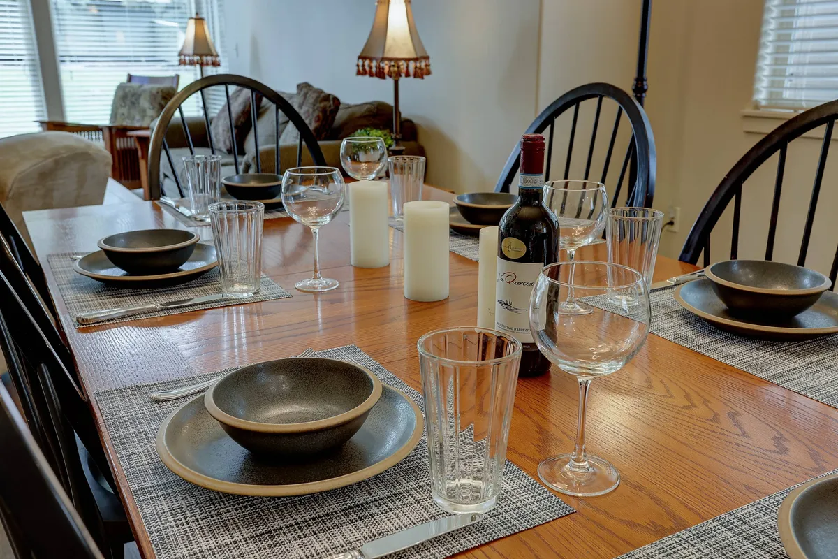 A close view of a dining table set with a wine bottle, glassware, dinner plates, and candles. The composition suggests a cozy, inviting atmosphere ideal for socializing, entertaining, and creating lasting memories over meals.