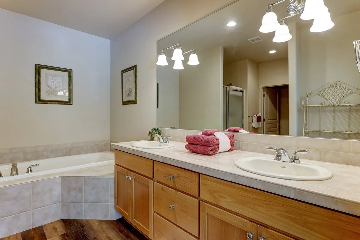 A spacious bathroom with double vanity sinks, a bathtub, neatly arranged towels, and soothing framed artwork creates an inviting, spa-like atmosphere for relaxation and self-care rituals.