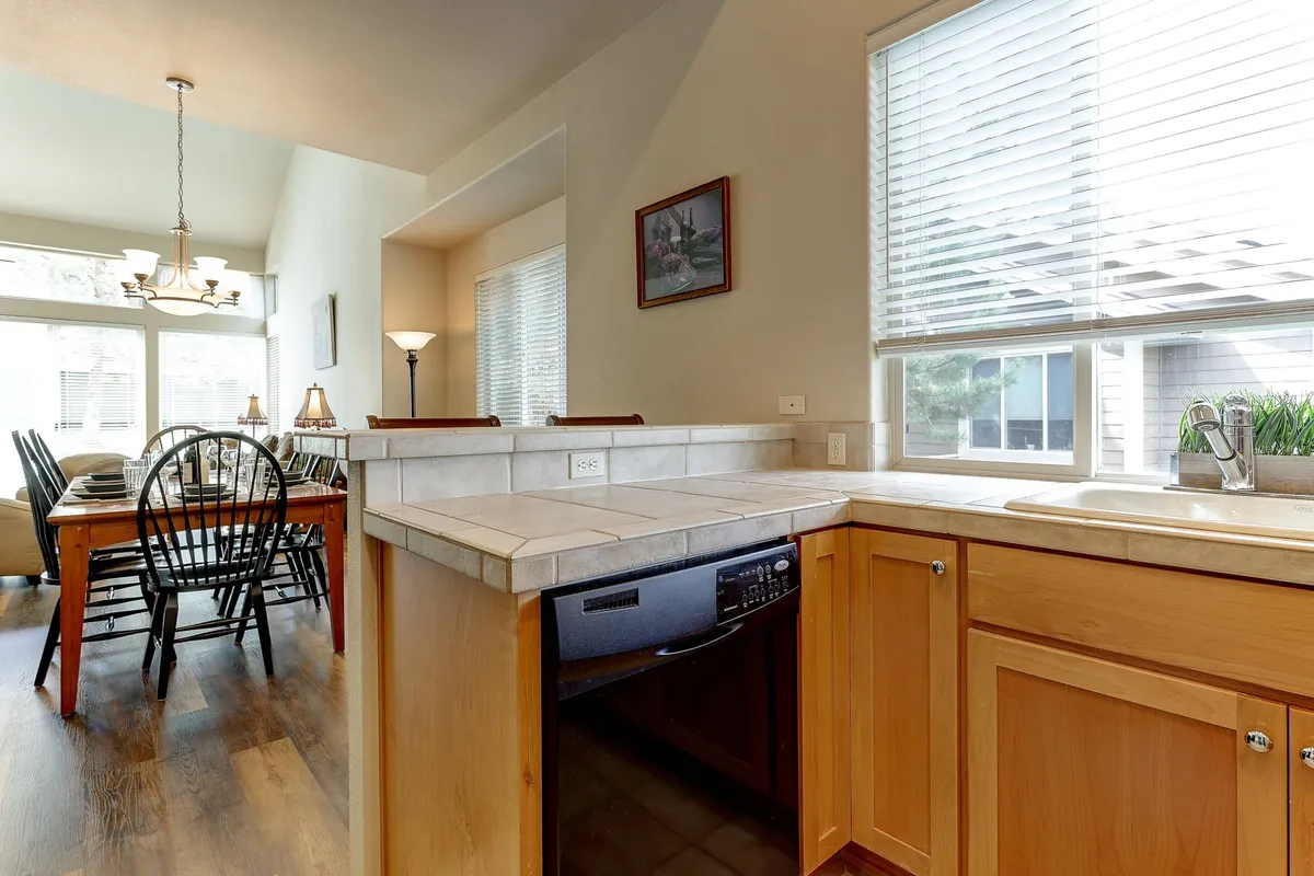 The image presents a kitchen counter with an adjacent dining table, positioned by a window that brings in natural light. The layout connects the kitchen and dining area, suggesting seamless transitions between cooking and dining activities. The mood feels warm and welcoming, suitable for celebrations or casual brunches.
