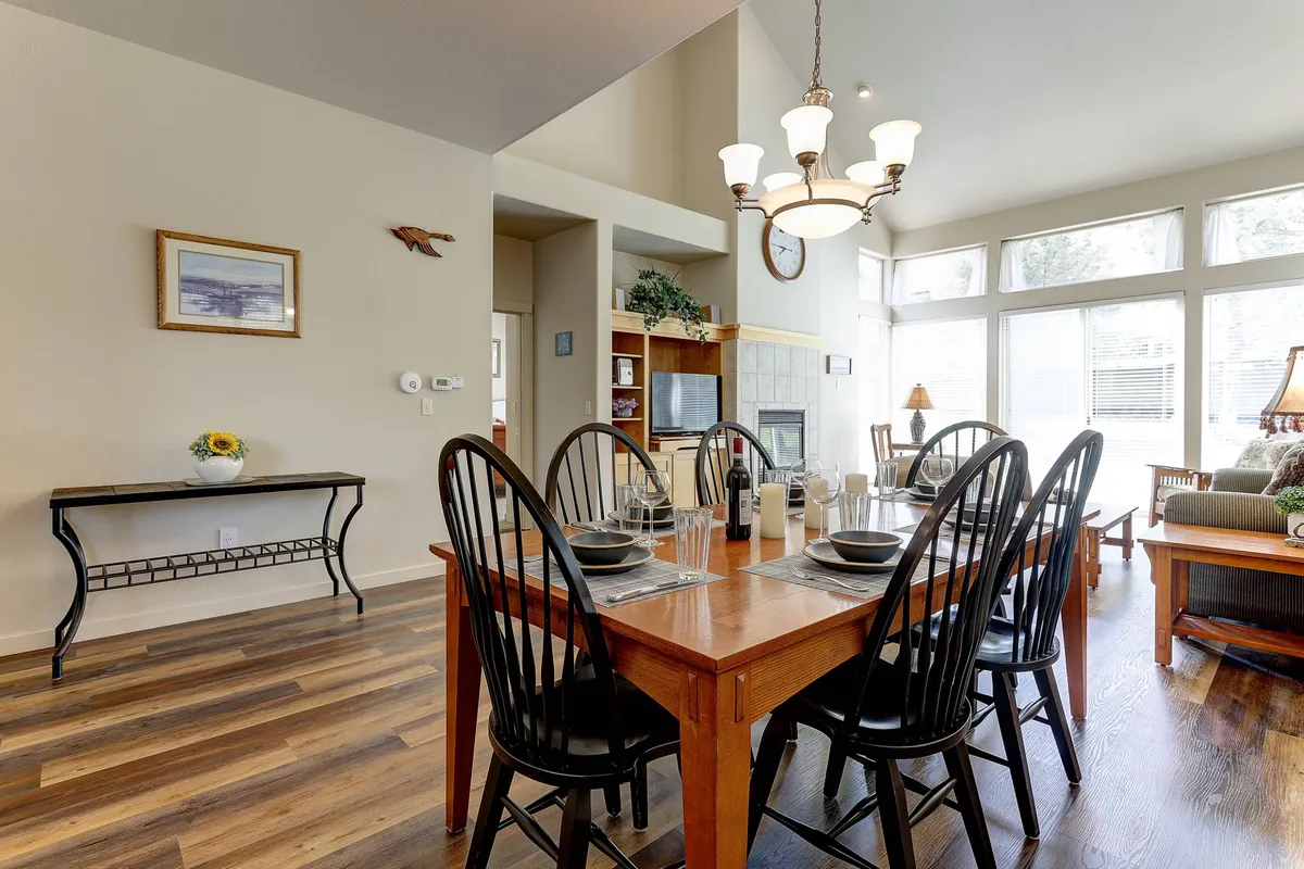 This image showcases a spacious, open-concept living and dining area with a plush sofa positioned near a glowing fireplace. Large windows bathe the room in Oregon sunlight, and a dining table sits under a stylish chandelier, creating an atmosphere ideal for both relaxing and socializing.