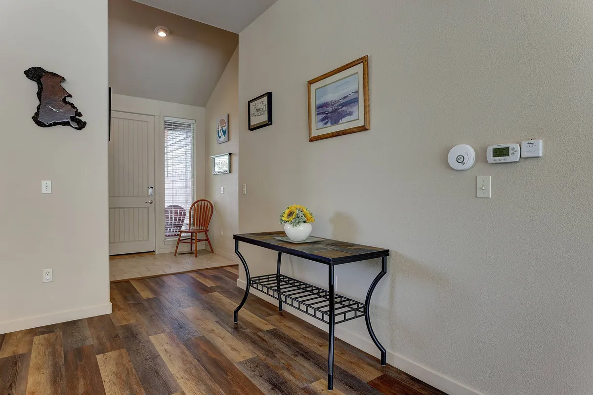 This image features the entrance door, a table adorned with flowers, artwork on the wall, and a wooden chair. The scene radiates a welcoming and inviting atmosphere that sets the tone for arriving guests.