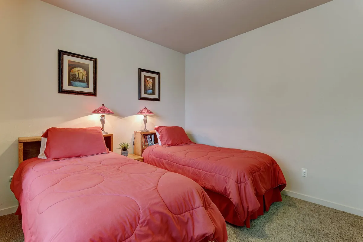 This scene shows a cheerful bedroom with two twin beds featuring bright red bedding, bedside lamps, and playful artwork on the walls, creating a cozy and welcoming environment for children or friends.