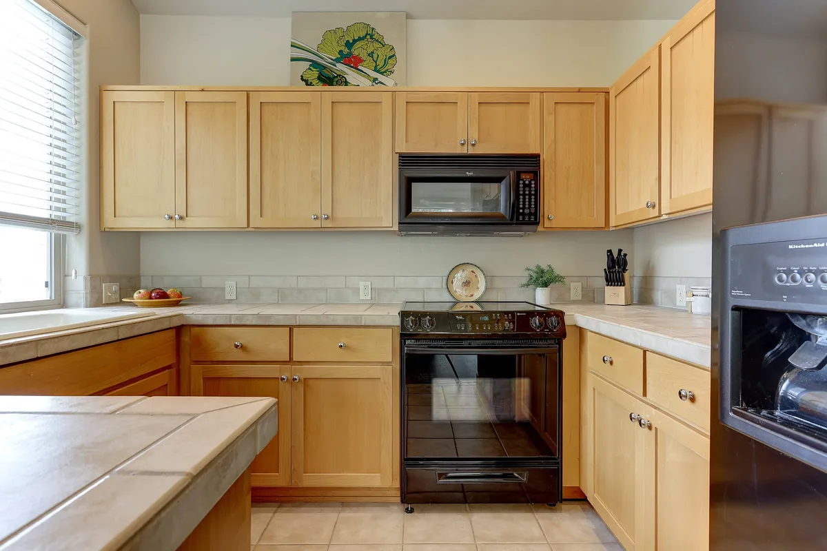 This image features a well-equipped kitchen with prominent cabinetry, a black stove, a microwave, and ample kitchen counter space. There is wall art adding personality, and the scene exudes a welcoming atmosphere, suggesting active meal preparation and family gatherings.