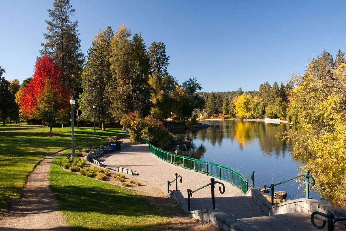 A tranquil lake framed by colorful trees, walking paths, and park benches, suggesting abundant outdoor recreation. The setting is serene yet vibrant, reflecting seasonal changes and opportunities for resort-style activities like walking, jogging, and enjoying nature.